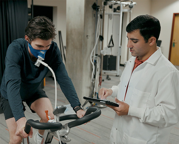 A student conducts physiology research with an athlete using a bicycle